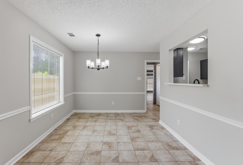 Dining space featuring tiled flooring, a multi-light chandelier, a large window with blinds, and decorative chair rail molding