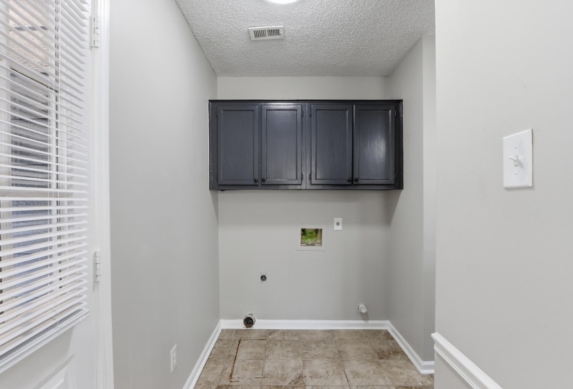 Dedicated utility space featuring overhead dark cabinetry, textured ceiling, tiled flooring, and light gray wall paint