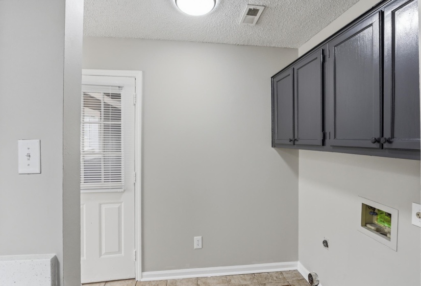 Utility room with a white exterior door, overhead gray cabinetry, tile-look flooring, and light gray walls