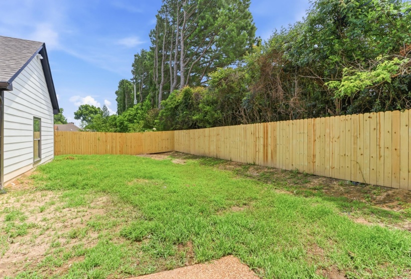 Spacious backyard featuring a new wood privacy fence, expansive lawn area, and mature perimeter trees