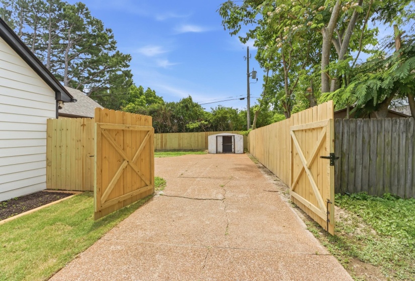 Gated property access with a concrete driveway, a privacy fence, and a storage shed