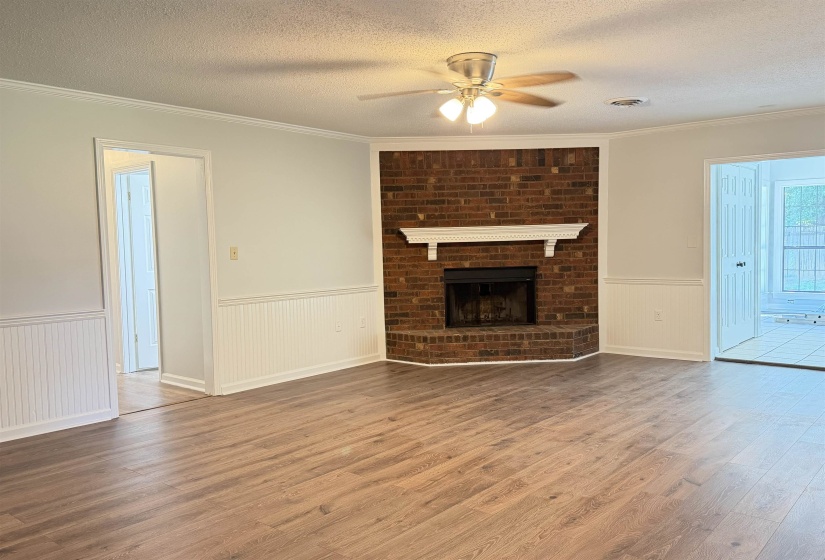 Spacious interior featuring wood-finish flooring, a brick fireplace with a white mantel, white beadboard wainscoting, and a ceiling fan with integrated lighting