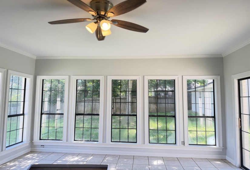 Room featuring a series of large gridded windows, crown molding, and a ceiling fan with integrated lighting