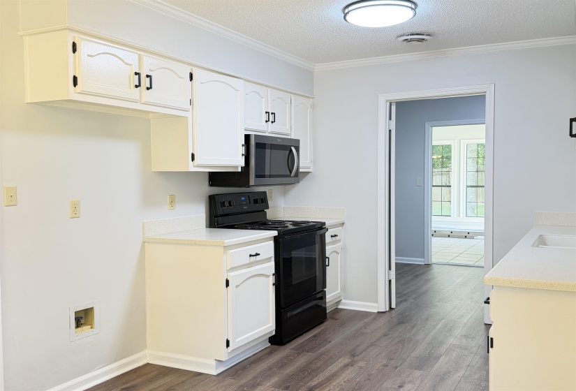 Kitchen featuring wood-finish flooring, white cabinetry with black hardware, and an overhead microwave