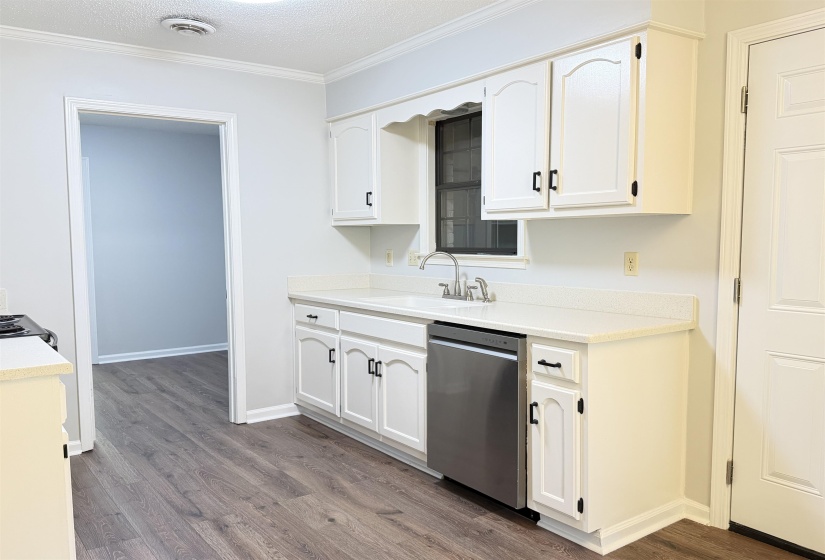 Kitchen featuring white cabinetry with black hardware, an integrated dishwasher, and wood-finish flooring