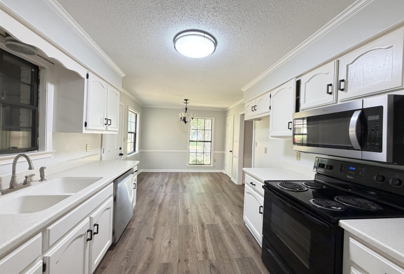 Kitchen featuring white cabinetry with black hardware, white countertops, wood-finish flooring, and stainless steel appliances including a microwave and dishwasher