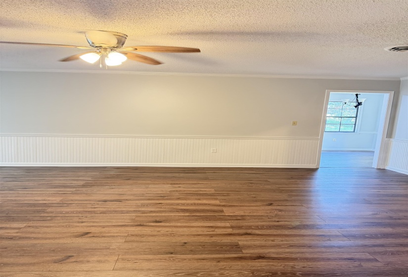 Spacious room featuring wood-finish flooring, white beadboard wainscoting, and crown molding