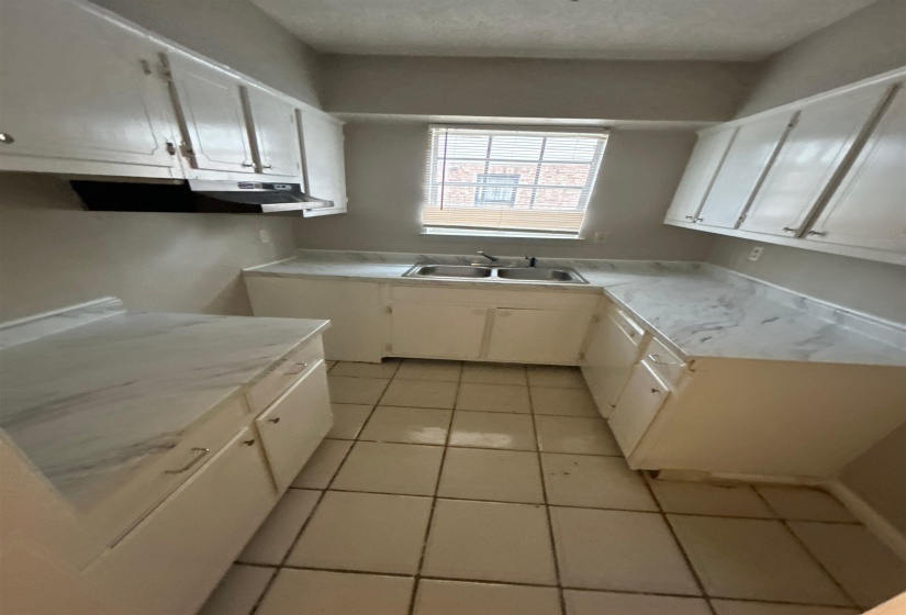 Kitchen featuring white cabinetry, a dual basin stainless steel sink, marbled countertops, and tile flooring