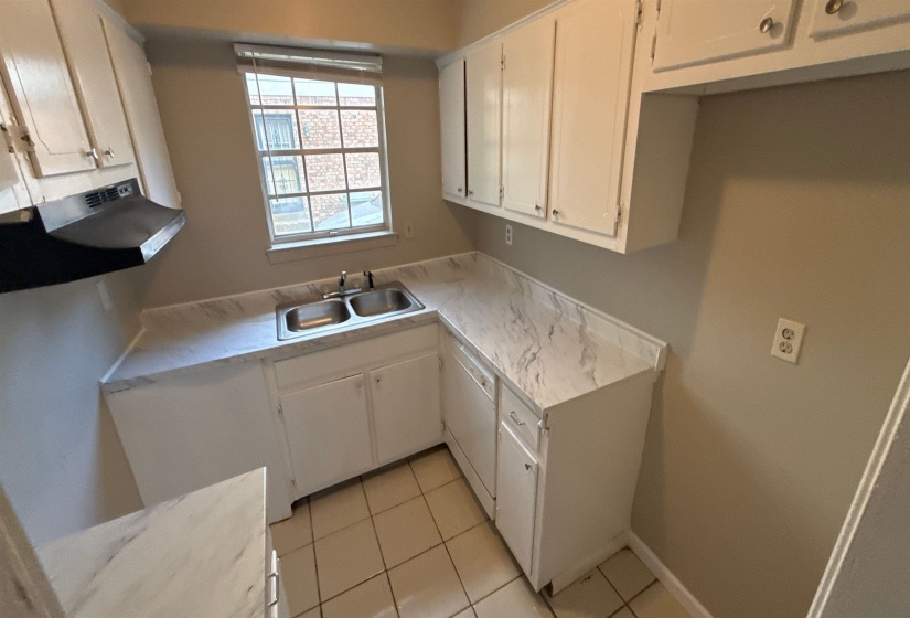 Functional kitchen featuring white cabinetry, a double basin stainless steel sink, marbled laminate countertops, a black range hood, and tile flooring