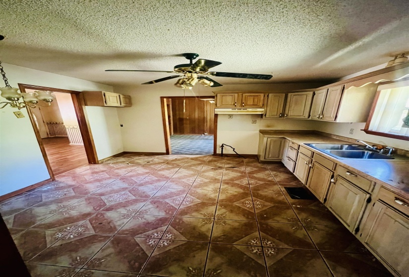 Kitchen with a ceiling fan, a textured ceiling, dark tile patterned floors, light countertops, and under cabinet range hood