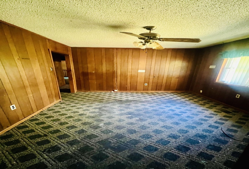 Empty room with wood walls, a textured ceiling, and a ceiling fan