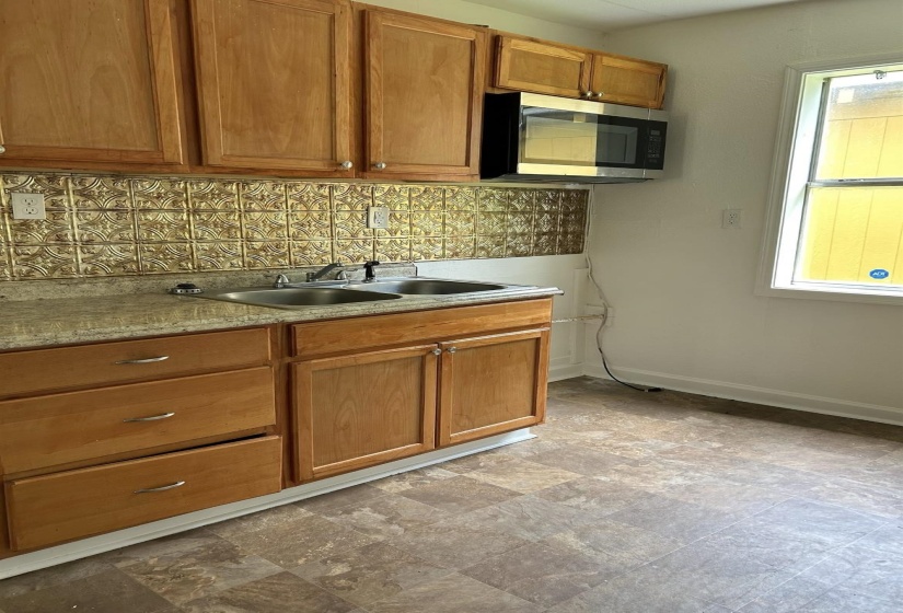 Kitchen with stainless steel microwave, wood finish cabinets, stone finish flooring, and tasteful backsplash