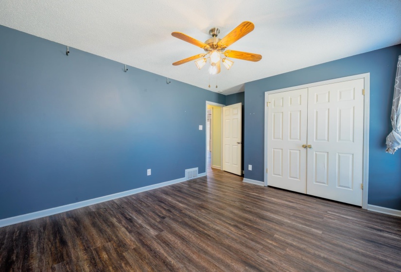 Room featuring wood-finish flooring, a ceiling fan with integrated lighting, and a double-door closet with paneling