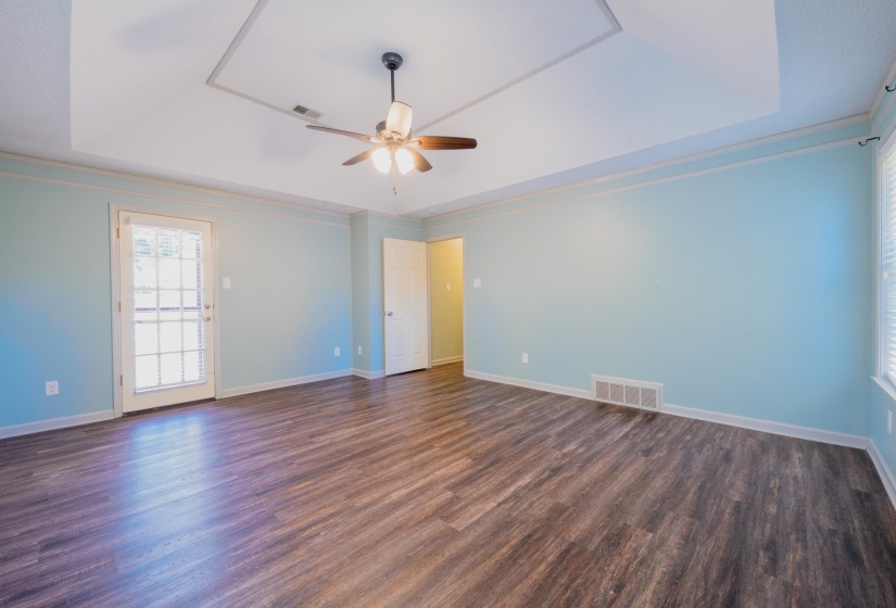 Spacious room with wood-finish flooring, a tray ceiling, and a ceiling fan