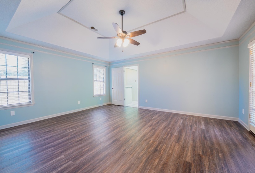 Spacious interior room featuring wood-finish flooring, a tray ceiling with a ceiling fan, and multiple windows with blinds