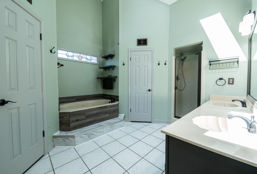 Bathroom featuring a soaking tub with wood-finish paneling, a stained-glass transom window, a separate shower enclosure, and a dual vanity with undermount sinks