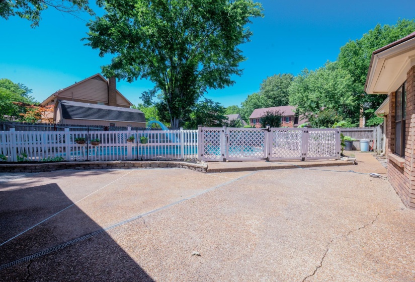 Expansive concrete patio area with brick exterior and a privacy-fenced in-ground swimming pool