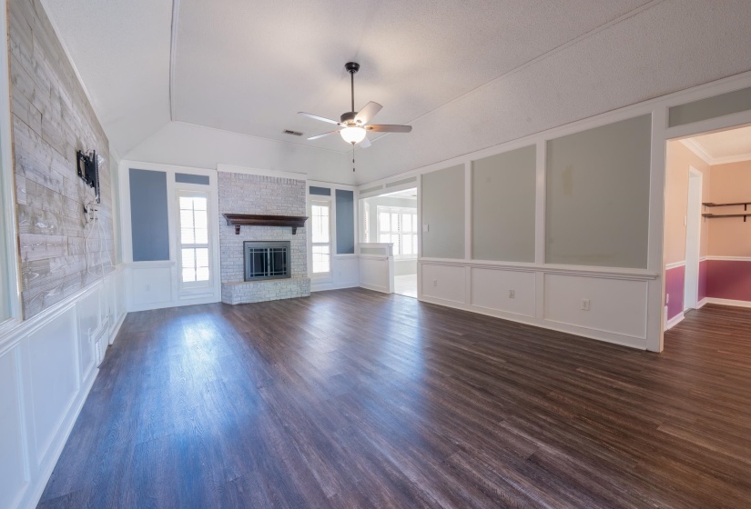 Spacious living area featuring wood-finish flooring, a white brick fireplace with a dark wood mantel, and wainscoting with accent panels