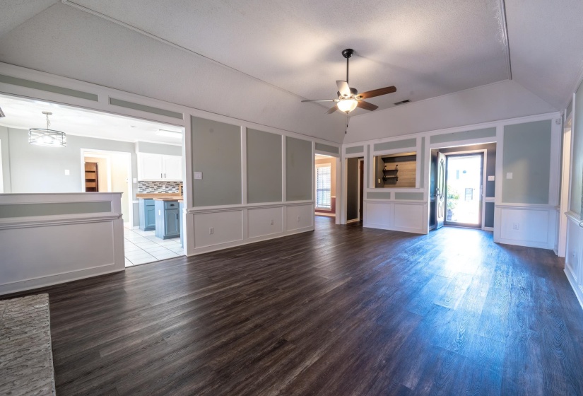 Spacious living area featuring dark wood-finish flooring, vaulted ceilings, and wainscoting with board and batten detailing