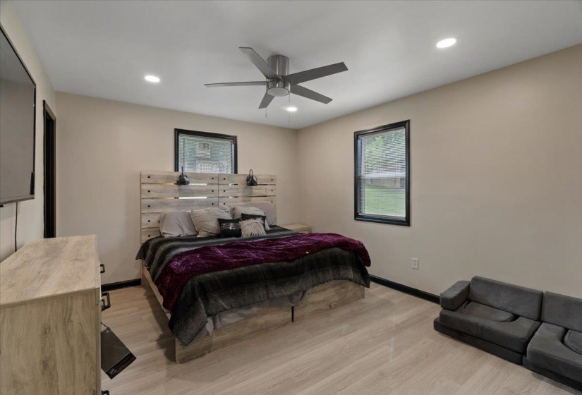 Bedroom featuring light wood-finish flooring, two large windows with black trim, recessed lighting, and a contemporary ceiling fan