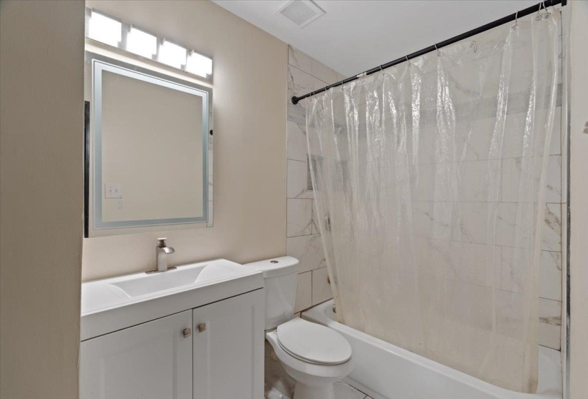 Full bathroom featuring a white vanity with integrated sink, rectangular framed mirror, and a white bathtub with tile surround