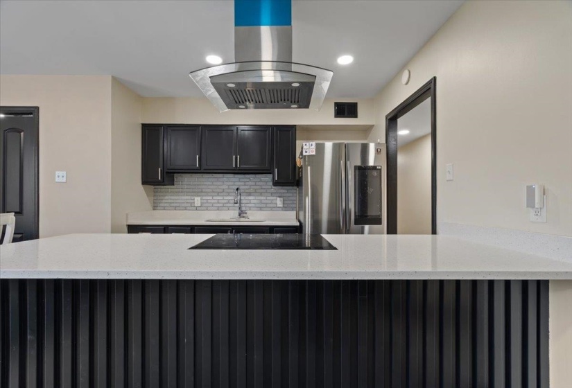 Kitchen featuring a black slatted island with white speckled countertops, black cabinetry, a stainless steel range hood, and a tile backsplash