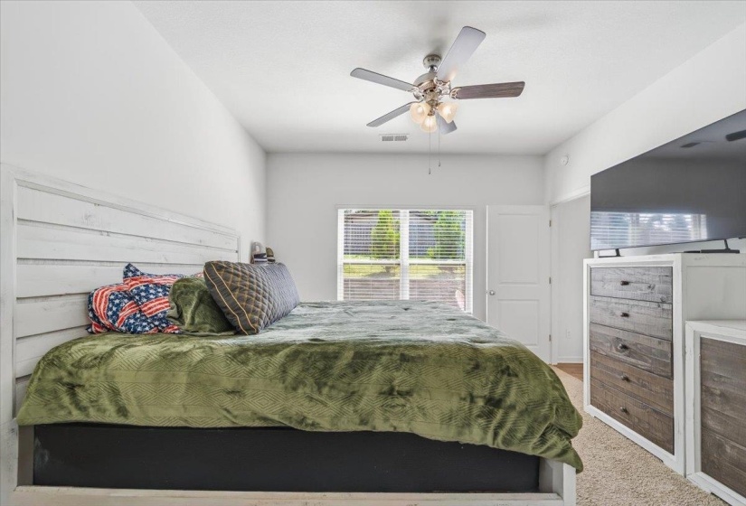 Carpeted room featuring a white paneled headboard, a window with horizontal blinds, and a white door