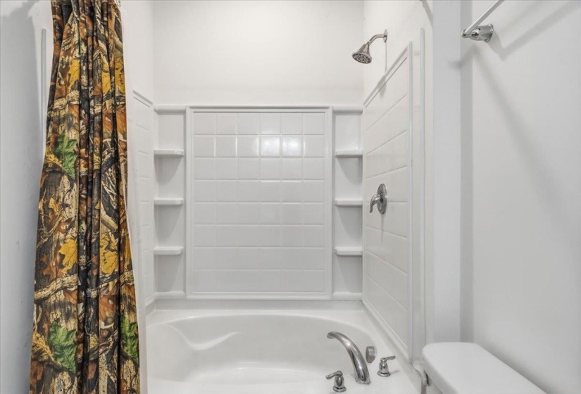 White bathtub with integrated shower, featuring a tiled surround and built-in shelving