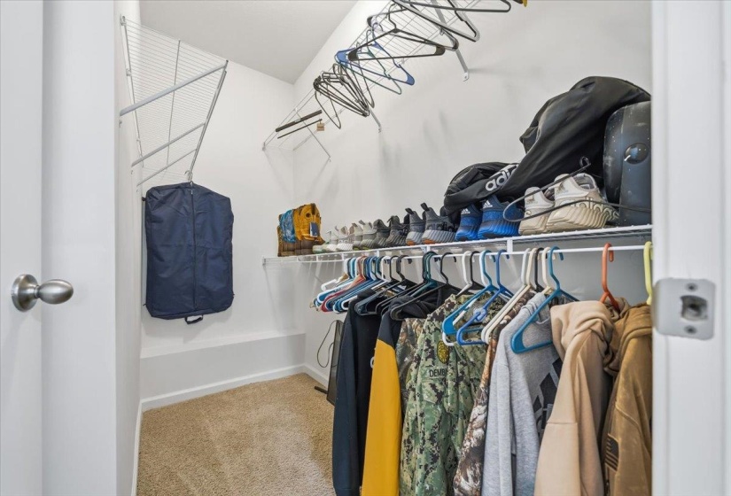 Carpeted closet space featuring wire shelving systems, multiple hanging rods, and white painted walls