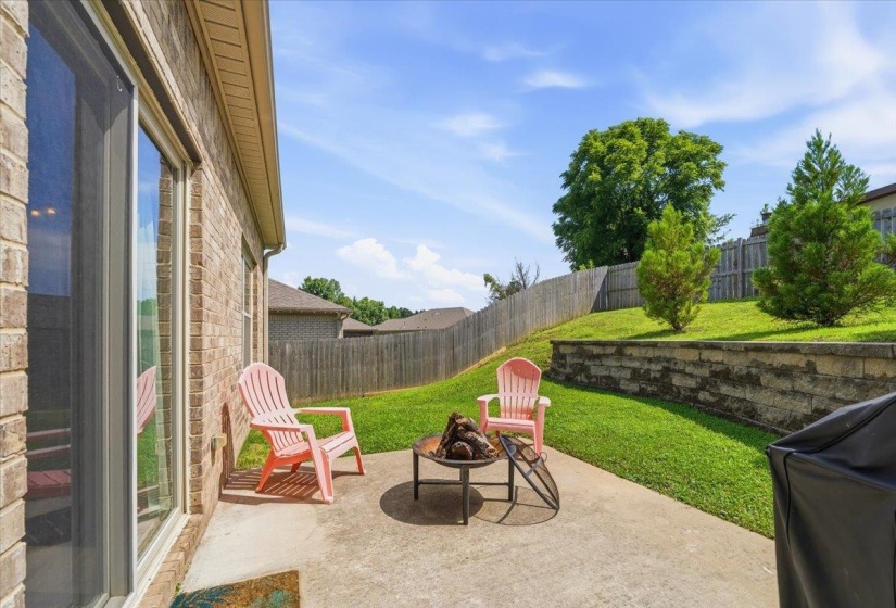 Backyard patio with a concrete surface, featuring a brick exterior, sliding glass door, tiered landscaping, and a privacy fence