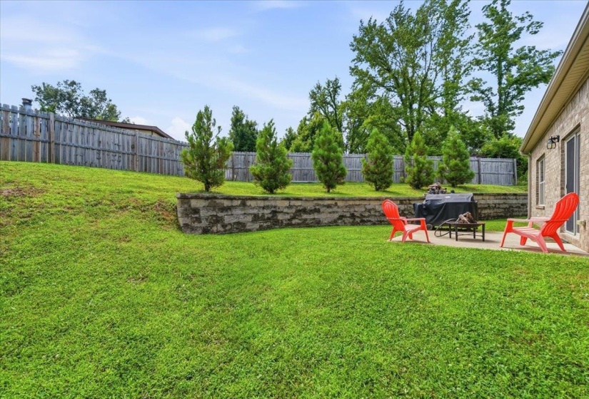 Expansive lawn featuring a retaining wall with mature plantings, a concrete patio, and a privacy fence