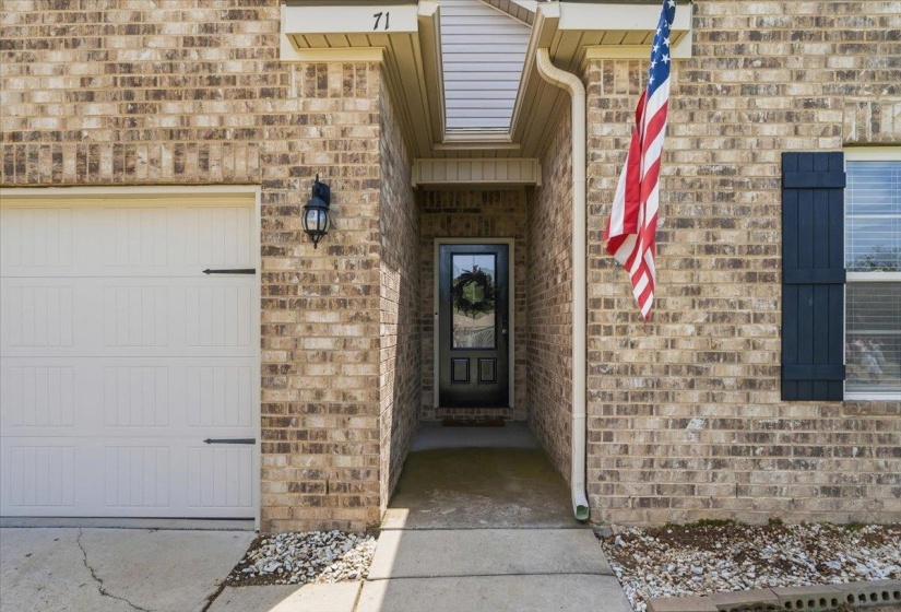 Brick exterior featuring a white paneled garage door with decorative hardware, dark shutters, a recessed entry, and an exterior wall lantern