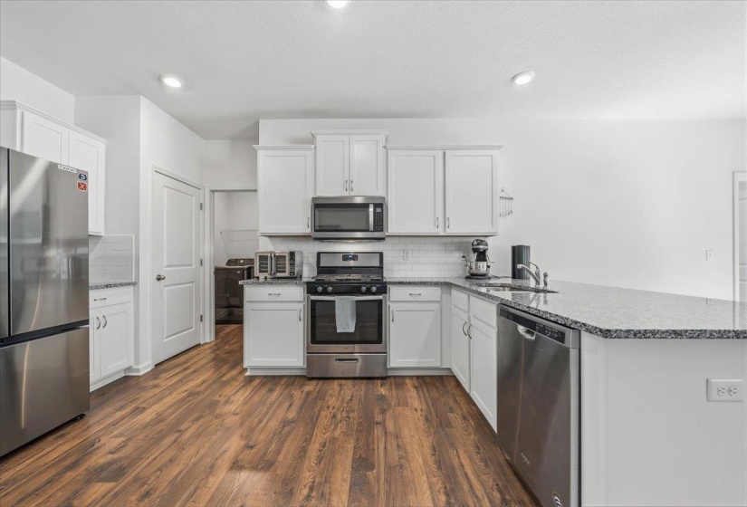 Well-appointed kitchen featuring wood-finish flooring, white cabinetry, stainless steel appliances, a subway tile backsplash, and a light-toned countertop