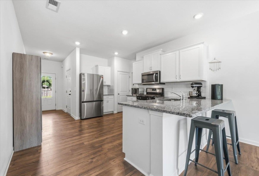 Modern kitchen featuring white cabinetry, stainless steel appliances, a subway tile backsplash, and a large island with a speckled countertop
