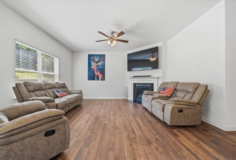Spacious living area featuring wood-finish flooring, vaulted ceilings, and a corner fireplace with a white mantel