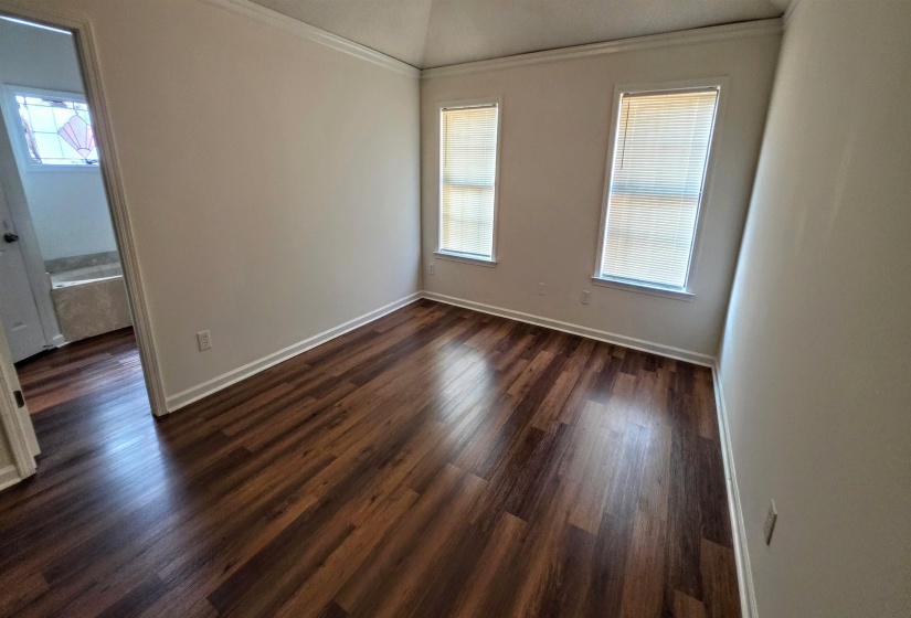 Spacious room featuring rich wood-finish flooring, crisp white walls, and elegant crown molding