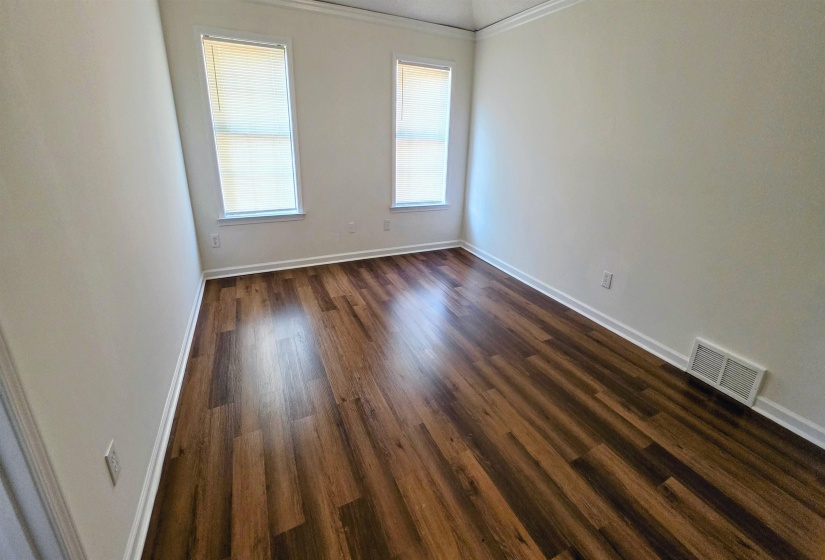 Spacious room featuring wood-finish flooring, two windows with blinds, crown molding, and white baseboards