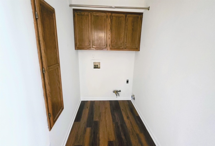 Laundry area with wood-finish flooring, overhead cabinetry, and a wall-mounted rod