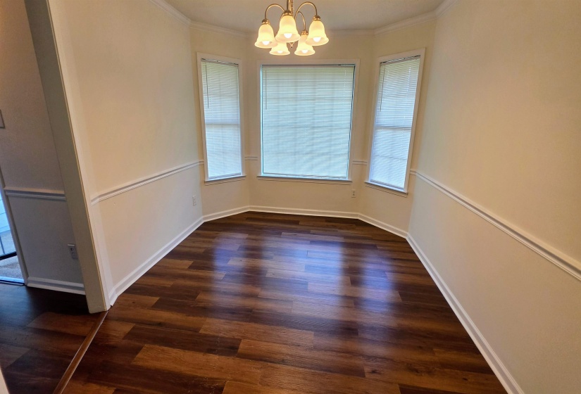 Dining area featuring wood-finish flooring, a bay window with blinds, decorative chair rail molding, crown molding, and a chandelier with frosted glass shades