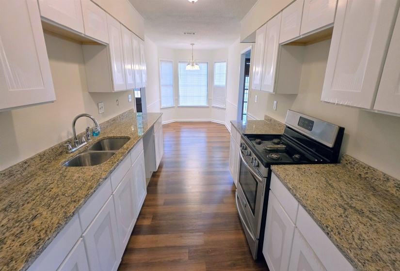 Kitchen with white shaker-style cabinetry, granite-style countertops, stainless steel appliances, a double basin sink, and wood-finish flooring