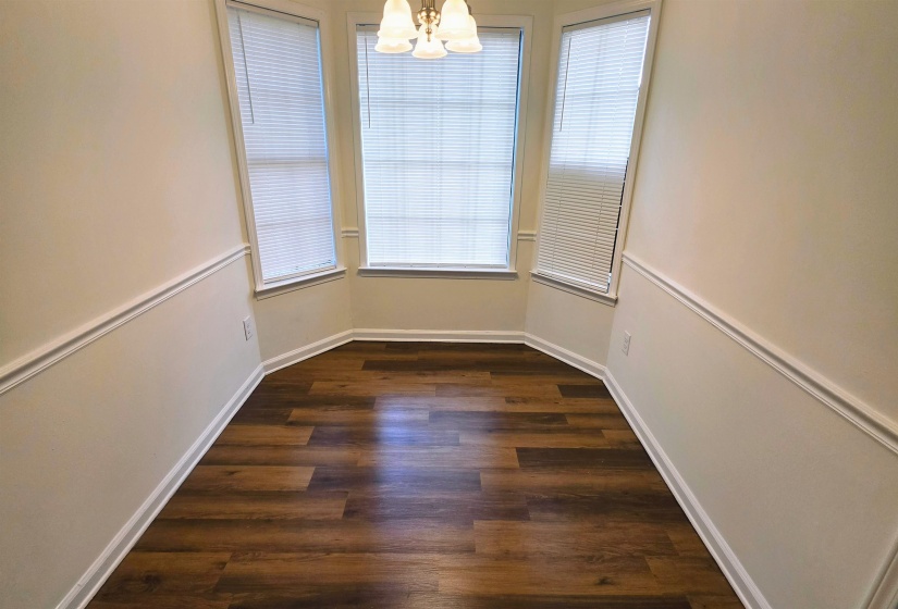 Bay window with multiple glass panes and blinds, wood-finish flooring, chair rail molding, and a four-light chandelier