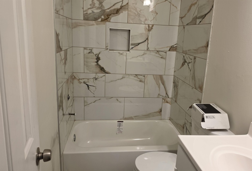 Bathroom featuring a white subway tile surround with brown veining, an integrated shower niche, and a white soaking tub