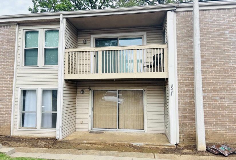 Two-story exterior featuring a private balcony with wooden railing, a ground-level patio, and light-colored siding