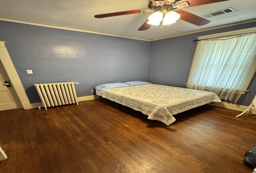 Room featuring wood-finish flooring, a ceiling fan with integrated lighting, and a window with blinds