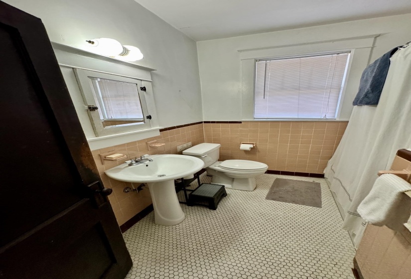 Bathroom featuring white hexagon tile flooring, a pedestal sink, and light peach wall tiling