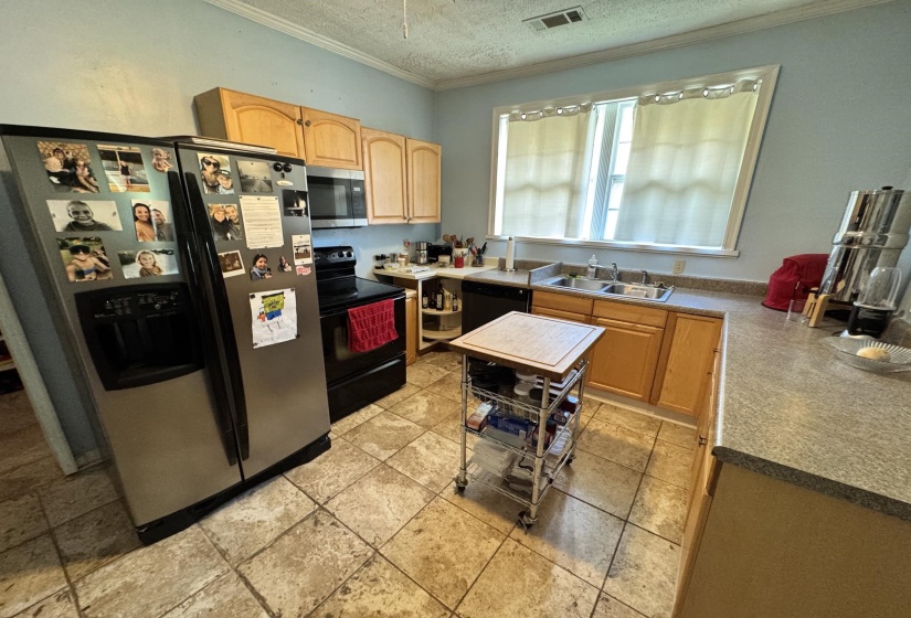 Kitchen featuring light wood cabinetry, a stainless steel refrigerator, black range, and a dual basin sink