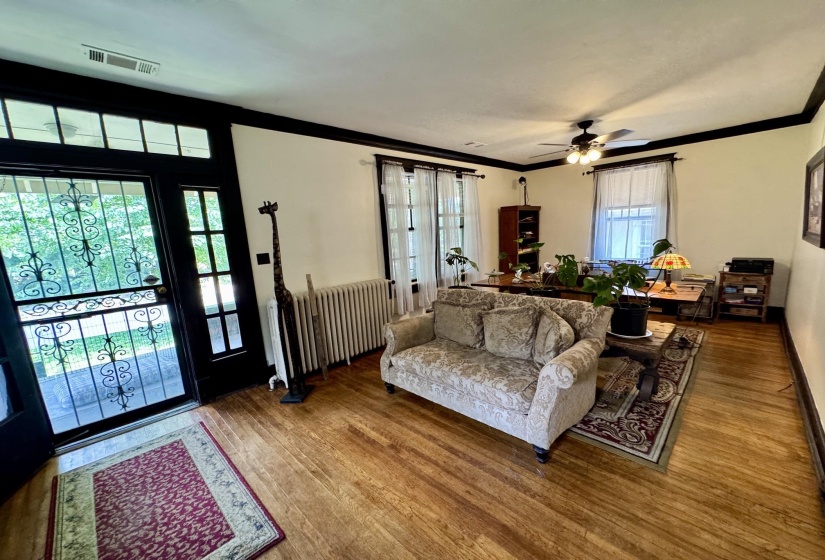 Open-concept living area featuring hardwood flooring, multiple windows providing natural light, a ceiling fan, and classic trim detailing