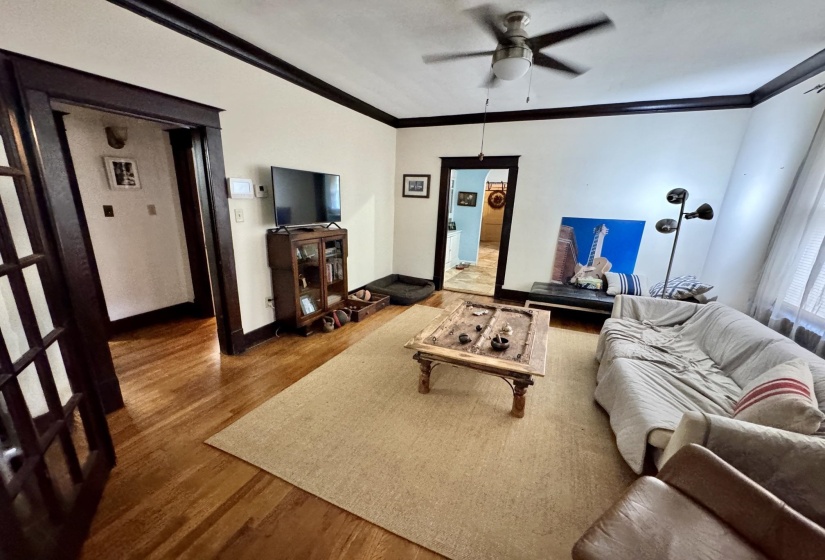 Living space featuring wood-finish flooring, dark wood trim, a ceiling fan with integrated lighting, and multiple doorways