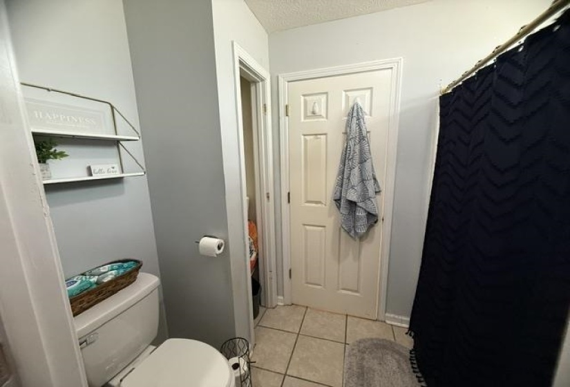 Bathroom featuring tile flooring, a built-in toilet, and a white two-tier wall shelf