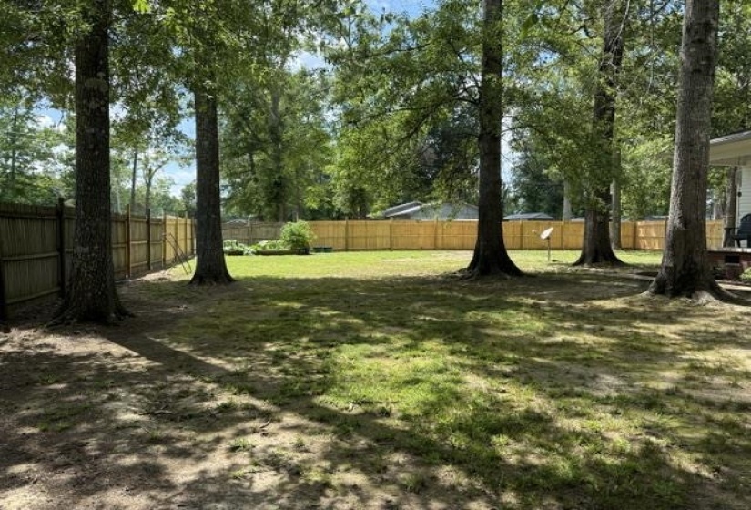 Expansive backyard featuring a natural grass lawn, mature trees, and a wooden privacy fence